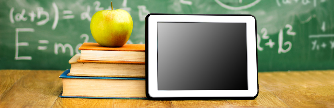 Green apple on 3 books next to a tablet in front of chalk board